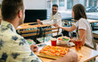 © David Pereiras - Happy young colleagues having lunch together in cafe, sharing pictures in smartphone while eating vegetarian pizza and poke bowl salad, enjoying break time. Healthy lifestyle and vegan food concept.