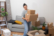 © olga_demina - A content and delighted woman moves to her new home, standing in the living room with a pile of cardboard relocation boxes, feeling at home