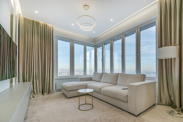 Panoramic view of the city from the window of a modern studio apartment. Elegant interior with a white sofa and a large carpet on the floor.