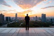 © kometa - Businessman overlooking modern city skyline during vibrant sunset inspirational moment of reflection and ambition on rooftop background for corporate vision poster or design project