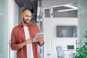 Successful satisfied businessman using tablet computer inside office at workplace, man in casual shirt reading online report, programmer developer testing new software.