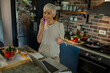 © Marko Geber - Senior woman cooking in kitchen while talking on phone