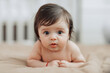 © Vasil - A baby is laying on a bed with its eyes wide open. The baby's face is the main focus of the image, and it is curious or surprised. The bed is covered in a brown blanket