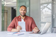 © Liubomir - Portrait of a young successful businessman at the workplace, man looking at the camera with a tablet computer in his hands, office worker using a laptop at work.