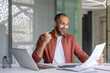 © Liubomir - Successful financier celebrating victory and success reading report. Man behind paperwork working with laptop inside office with documents, businessman in shirt got winning investment results.