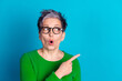 © deagreez - Surprised mature woman with gray hair pointing sideways against bright blue background