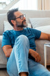 © simona - A 50-year-old man sitting on the floor in his living room, wearing casual clothes, using a laptop placed on a small table to browse the web, engage with social media, and work online during