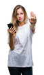 © Krakenimages.com - Young beautiful blonde woman using smartphone over isolated background with open hand doing stop sign with serious and confident expression, defense gesture