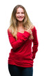 © Krakenimages.com - Young beautiful blonde woman wearing red sweater over isolated background cheerful with a smile of face pointing with hand and finger up to the side with happy and natural expression on face.