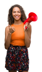 Wall Mural - Young hispanic woman holding megaphone happy with big smile doing ok sign, thumb up with fingers, excellent sign