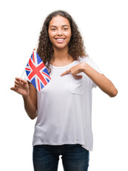 Wall Mural - Young hispanic woman holding flag of United Kingdom with surprise face pointing finger to himself