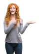 © Krakenimages.com - Young redhead woman amazed and smiling to the camera while presenting with hand and pointing with finger.