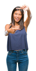 Wall Mural - Young asian woman over isolated background smiling making frame with hands and fingers with happy face. Creativity and photography concept.