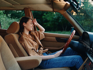 Canvas Print - Young woman enjoying a moment of relaxation in a vintage car, wearing a brown oversized shirt and jeans, surrounded by green nature, conveying a sense of freedom and tranquility.