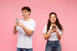 © Home-stock - Online communication. Happy European couple using smartphones, reading pleasant messages, chatting online and smiling over pink background