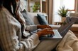 © ThomasLENNE - Young woman sitting on a sofa typing on a laptop