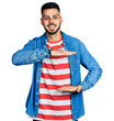 © Krakenimages.com - Young hispanic man with beard wearing casual denim jacket gesturing with hands showing big and large size sign, measure symbol. smiling looking at the camera. measuring concept.