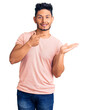 © Krakenimages.com - Handsome latin american young man wearing casual clothes amazed and smiling to the camera while presenting with hand and pointing with finger.