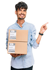 Wall Mural - Young hispanic man holding delivery package smiling happy pointing with hand and finger to the side