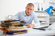 © JackF - Shocked young businessman overworked sitting at office table with many folders of papers