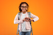 © Prostock-studio - I Love To Study. Portrait of smiling African Amercian girl making heart shape with her hands and fingers near chest, pupil wearing backpack and glasses, posing on yellow studio background, copyspace