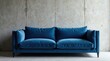 © parichart - A plush, deep blue velvet sofa rests against a textured concrete wall, offering a sophisticated and modern living room aesthetic.