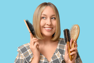 Wall Mural - Beautiful young woman with bob hairstyle holding hair brushes on blue background