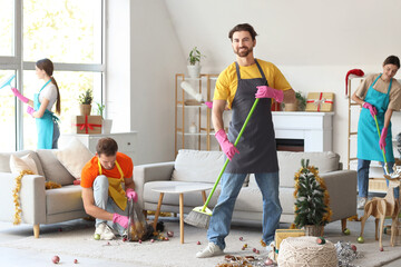 Canvas Print - Male janitor with broom and his team cleaning in room after New Year party