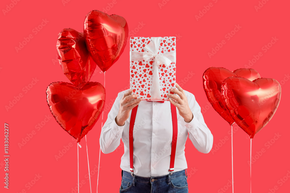 Mature man with gift box and heart-shaped balloons on red background. Valentine's Day celebration