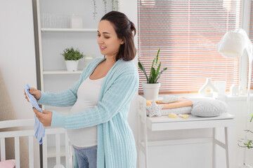 Canvas Print - Young pregnant woman with baby bodysuit in children's bedroom