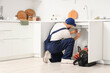 © Pixel-Shot - Male plumber repairing sink pipe in kitchen