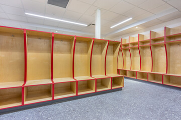 Empty team locker, changing room with traditional open wooden lockers with a red trim.