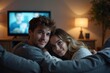 © Paull - Young couple cuddling on the sofa and watching movie on TV at home.