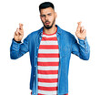 © Krakenimages.com - Young hispanic man with beard doing fingers crossed luck gesture in shock face, looking skeptical and sarcastic, surprised with open mouth