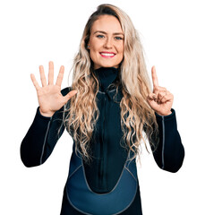 Wall Mural - Young blonde woman wearing diver neoprene uniform showing and pointing up with fingers number six while smiling confident and happy.