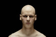 © Seventyfour - Portrait of unemotional pale man with with bald head staring at camera with scary gaze standing in hard light against black background in studio amplifying chilling atmosphere, copy space