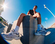 © Studio Marmellata - A low-angle fisheye view of a young man in athletic attire seated on a concrete ledge in an urban environment with clear skies and bright sunlight in the background.