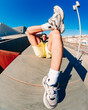 © Studio Marmellata - A fisheye view of a man reclining on a modern concrete structure under a vibrant blue sky, emphasizing his sneakers and legs, with urban architecture and a streetlight in the background.