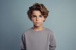 © MediaRaw - A boy with short hair and a gray sweater is standing in front of a blue wall