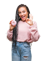 Wall Mural - Young african american girl eating pink donut over isolated background doing ok sign with fingers, excellent symbol