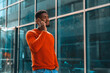© Iryna - Man in orange sweater talking on phone outside modern glass building during daytime