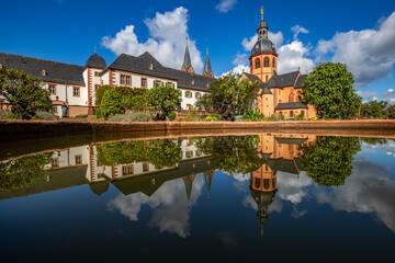 Wall Mural - A historic monastery in the morning. Monastery walls, church and buildings are reflected in the water of a fountain. Beautiful garden in Seligenstadt Monastery, Germany