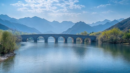 Wall Mural - Ancient stone bridge spans tranquil lake, mountain backdrop, serene spring scene