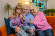 © Andrii Iemelianenko - Caucasian girl teaching elderly grandfather grandmother using smartphone on sofa in living room. Grandparents watching granddaughter play games on mobile phone. Happy family at home during weekends