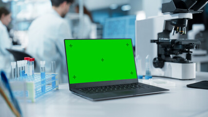 Aufkleber - Laptop Computer with Green Screen Mock Up Display Standing on a Table in a Science Laboratory Next to a Microscope and Test Tubes with Biological Samples. Anonymous People Working in the Background
