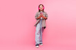 © deagreez - Young girl enjoying music on headphones with a pink background, wearing casual clothes and holding a smartphone.