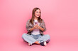 © deagreez - Adorable preteen girl seated against a pink background holding a smartphone with a cheerful expression