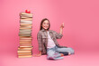 © deagreez - Cheerful young girl with books and a red apple on a vibrant pink background