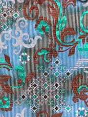 Wall Mural - Close up of ethnic sewn fabric in random ornamental swirls pattern. Traditional hand sewn and weaving fabric in floral and swirls shape, diamonds, and foliage leaves. Blue, tosca, and brown color.