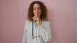 © Krakenimages.com - Woman doctor with curly brunette hair gestures for silence against an isolated pink wall background suggesting secrecy and confidentiality in healthcare.